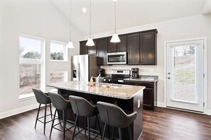 A modern kitchen with dark wood cabinets, a granite countertop, and a central island with bar stools. - Whip-Poor-Will-Cottage | Hocking Hills, 16 Acres (McArthur)
