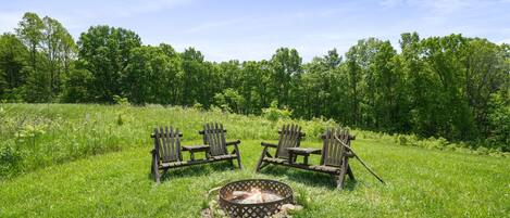 A grassy field with a fire pit and wooden chairs.