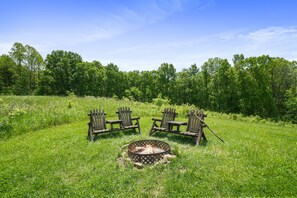 A grassy field with a fire pit and wooden chairs.