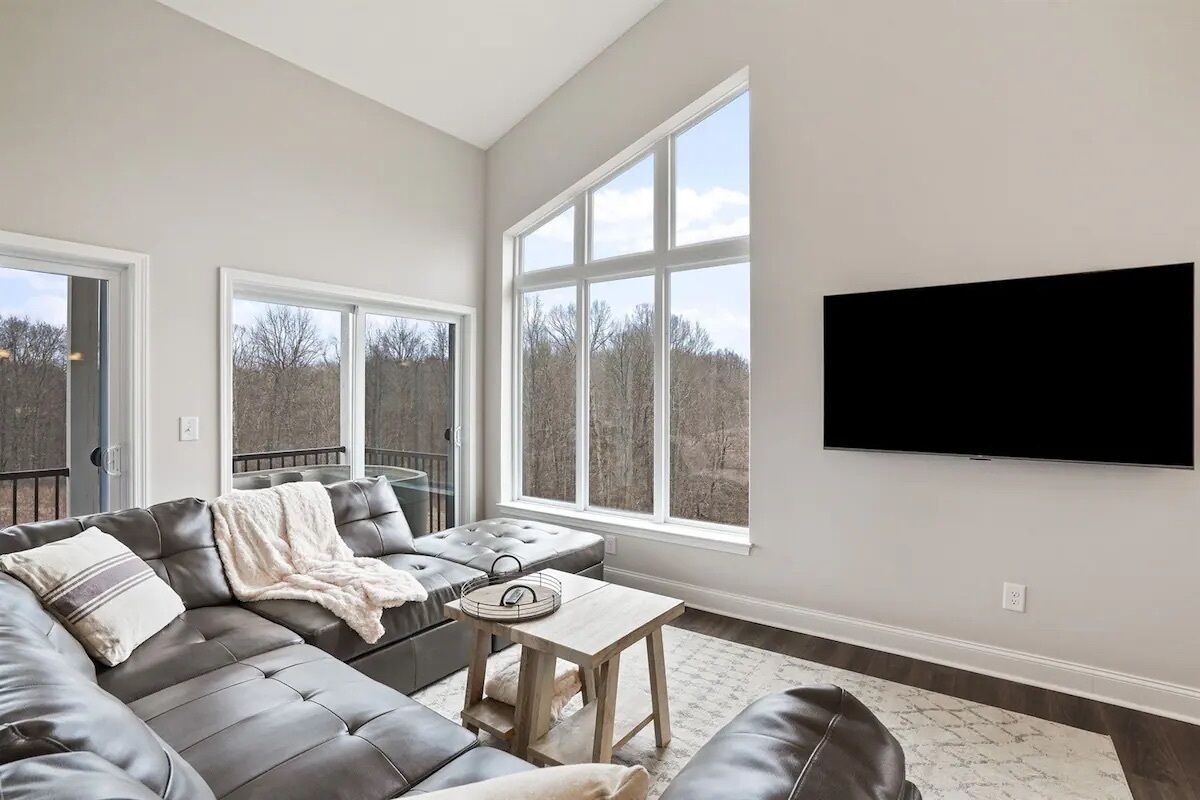 Un salon moderne avec un canapé d’angle en cuir, une table basse et une grande fenêtre donnant sur la verdure.