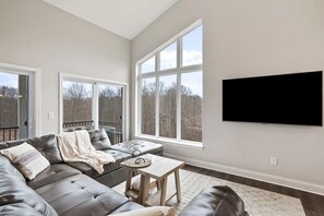 A modern living room with a leather sectional sofa, a coffee table, and a large window offering a view of trees.