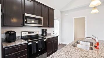 A modern kitchen with dark wood cabinets, stainless steel appliances, granite countertops, and a double sink.