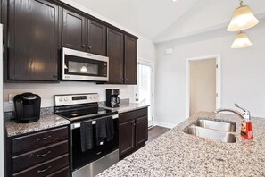 A modern kitchen with dark wood cabinets, stainless steel appliances, granite countertops, and a double sink.