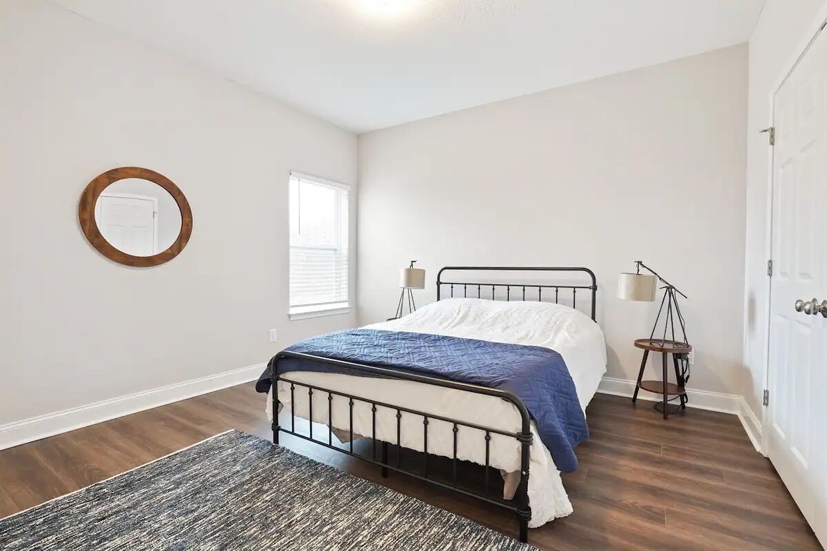A bedroom with a bed, a round mirror, a lamp, and a door.