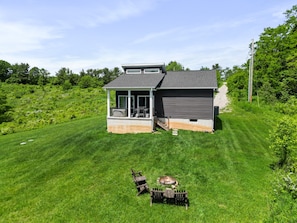 A modern house with a covered patio, a small deck, and a fire pit in the yard.