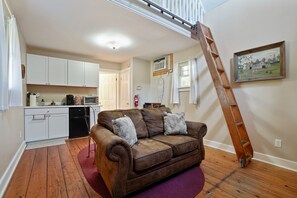 A cozy living room with a brown leather sofa, a purple rug, and a wooden ladder leaning against the wall.