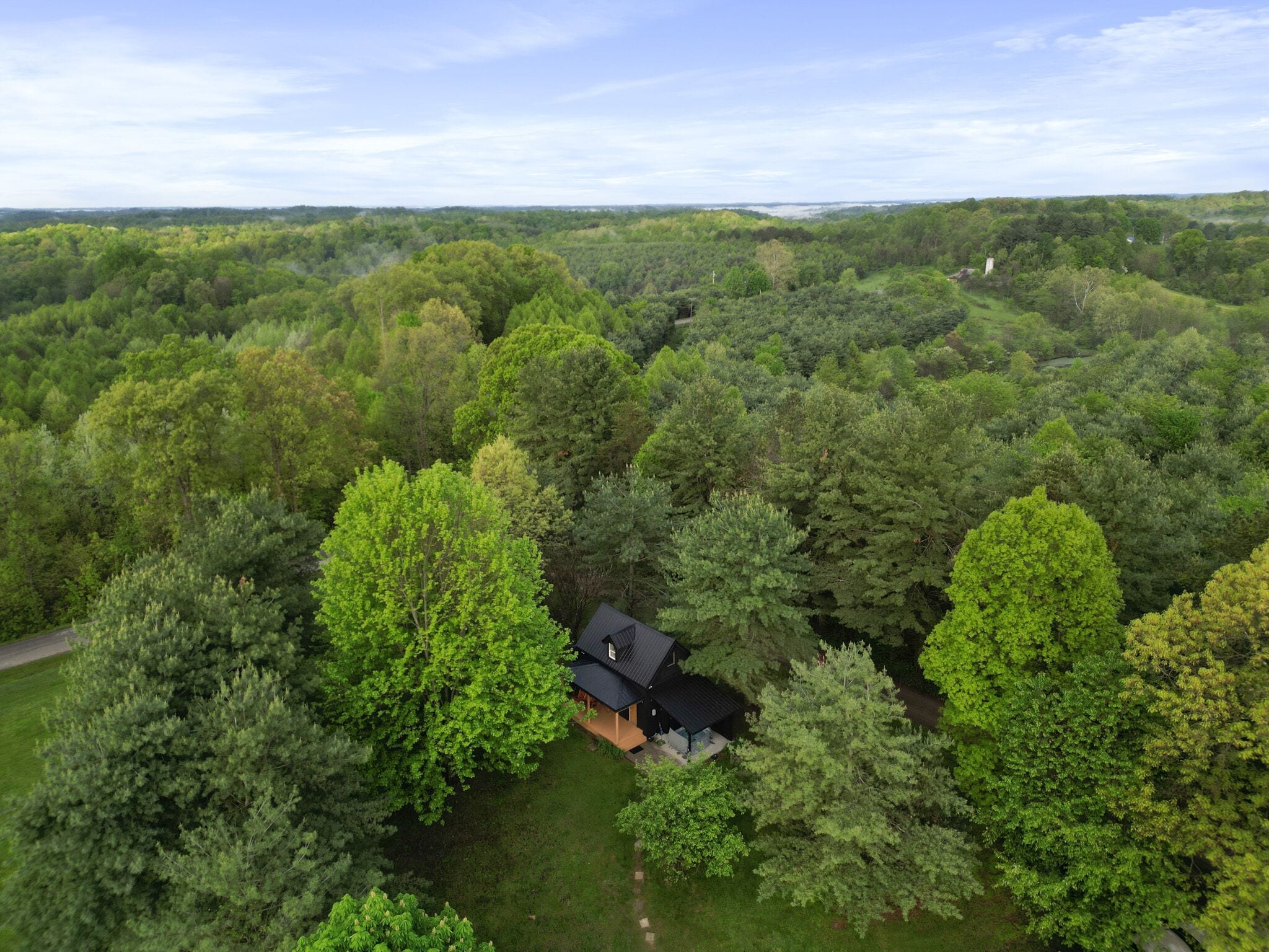 A house surrounded by dense forest, with a clear sky above.
