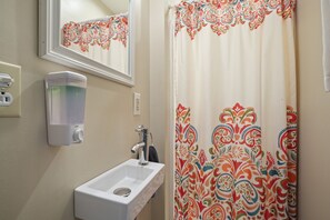 A bathroom with a white sink, a mirror, a soap dispenser, and a shower curtain with a colorful pattern. - Love Shack Cabin | Hocking Hills, Couples Retreat (McArthur)