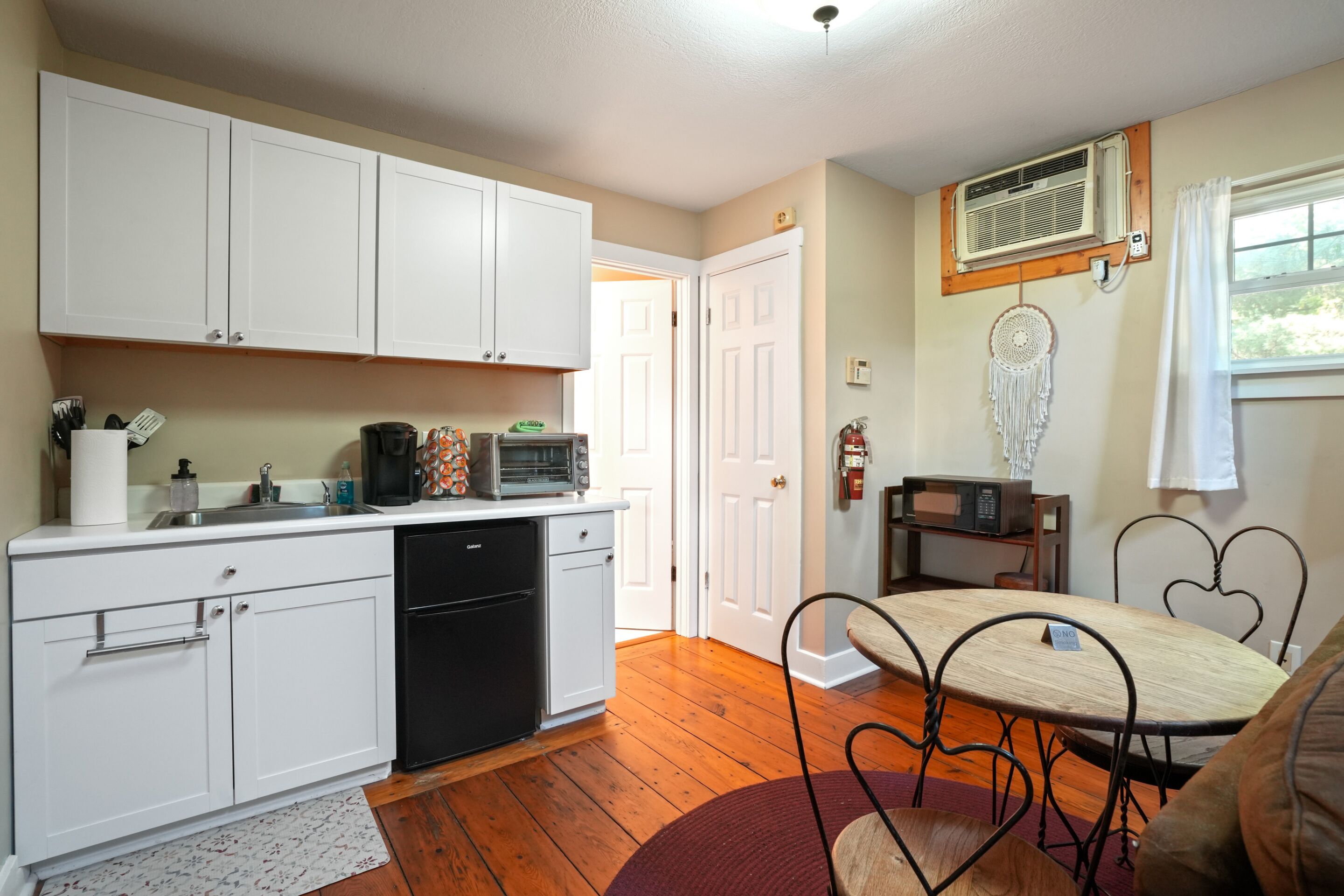 A compact kitchen with white cabinets, a black dishwasher, and a dining area with a heart-shaped metal table.