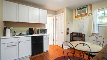 A compact kitchen with white cabinets, a black dishwasher, and a dining area with a heart-shaped metal table.