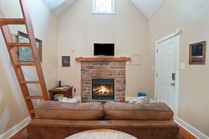 Un salon chaleureux avec une cheminée en pierre, une échelle en bois et un confortable canapé marron.