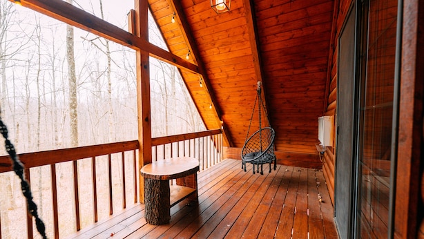 A wooden deck with a bench and a chair, a window, and a hanging light fixture. - Oak Cabin | Hocking Hills, Romantic Hot Tub (New Plymouth)