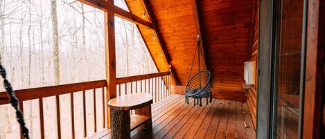 Une terrasse en bois avec un banc et une chaise, une fenêtre et un luminaire suspendu.
