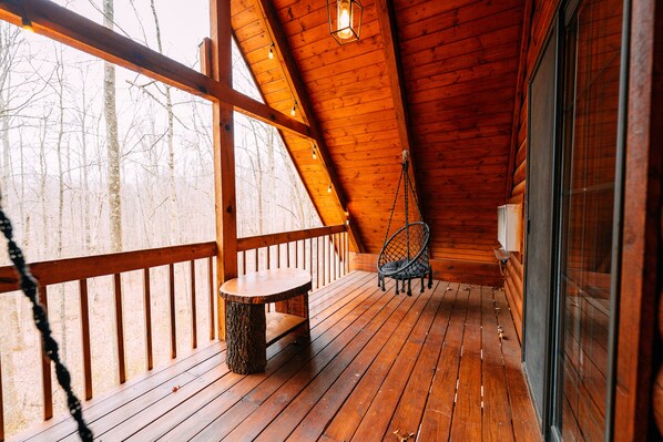 A wooden deck with a bench and a chair, a window, and a hanging light fixture.