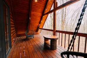 Une terrasse en bois avec une balançoire en corde, une table ronde et un fauteuil suspendu.