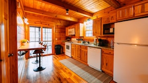 A wooden cabin interior with a kitchen, dining area, and a window. - Oak Cabin | Hocking Hills, Romantic Hot Tub (New Plymouth)