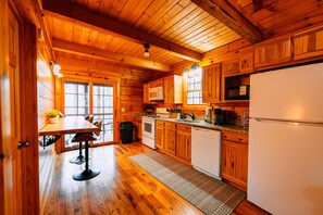 A wooden cabin interior with a kitchen, dining area, and a window.