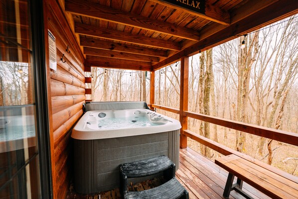Une cabane en bois avec un jacuzzi, une terrasse en bois et une vue sur les arbres.