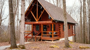 A log cabin with a porch, windows, and a staircase leading to the entrance. - Oak Cabin | Hocking Hills, Romantic Hot Tub (New Plymouth)