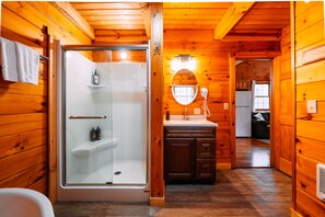 Un baño de cabaña de madera con ducha envuelta en vidrio, armarios de madera y un lavabo con espejo.