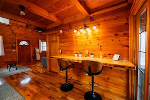 L’intérieur d’un chalet en bois comprend un bar, deux tabourets de bar, un plafond en bois et une fenêtre.