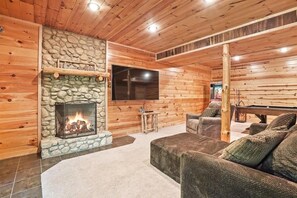 A cozy log cabin interior with a stone fireplace, a flat-screen TV, and a pool table.