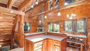 L’intérieur d’une cabane en rondins comprend un îlot de cuisine, un coin repas et de grandes fenêtres.