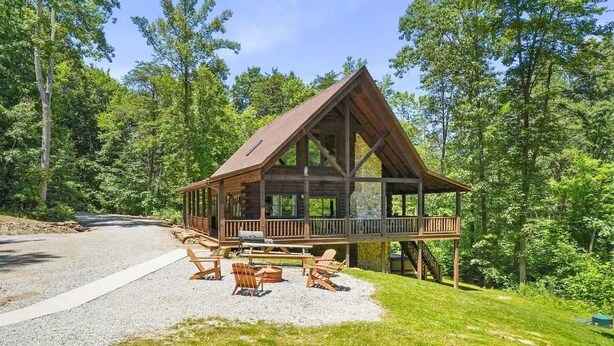 A wooden cabin with a deck, outdoor seating, and a gravel driveway. - Grizzly Ridge | Hocking Hills, Pool, Hot Tub (Logan)