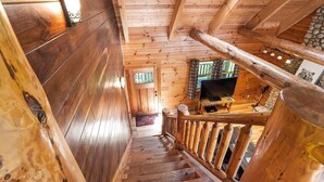 A wooden staircase leading to a room with a television and a stone wall. - Grizzly Ridge | Hocking Hills, Pool, Hot Tub (Logan)