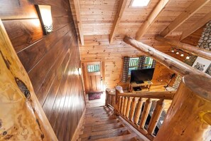 A wooden staircase leading to a room with a television and a stone wall.