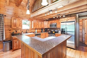 A modern kitchen with wooden cabinetry, stainless steel appliances, and a granite island.