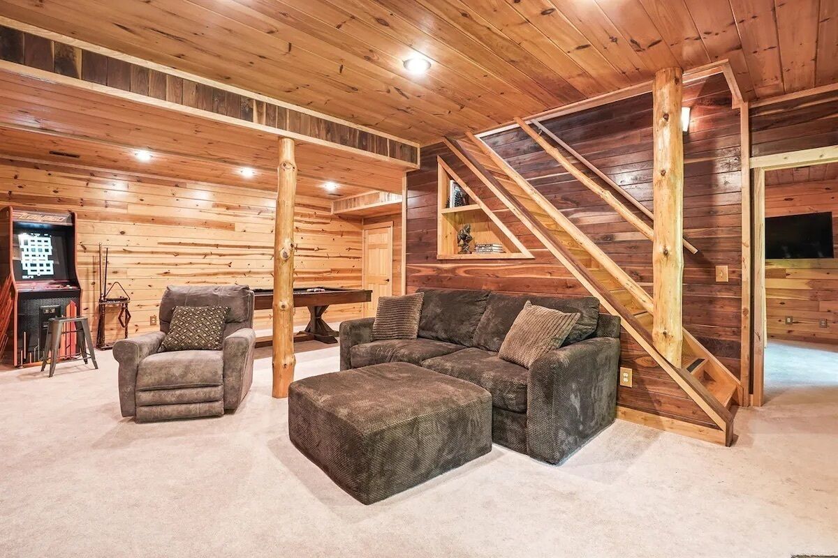 Un acogedor interior de cabaña de madera con un sofá seccional, un sillón reclinable y una escalera.