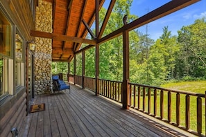 Eine Holzterrasse mit einer Steinmauer, einem blauen Stuhl und Blick auf einen Wald.