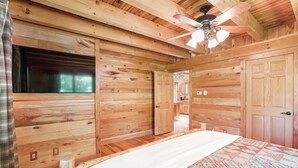 Une chambre de style cabane en bois, avec un lit, un ventilateur de plafond et une fenêtre.