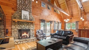 L’intérieur chaleureux d’un chalet avec une cheminée en pierre, des meubles en cuir et un plafond en bois.