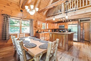 A rustic cabin interior with a wooden dining table, chairs, a kitchen with modern appliances, and a balcony. - Grizzly Ridge | Hocking Hills, Pool, Hot Tub (Logan)