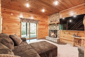 A cozy log cabin interior with a stone fireplace, a large flat-screen TV, and a comfortable sofa.