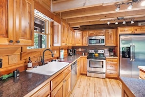 Eine Küchenzeile im Chalet-Stil mit einem großen Spülbecken, Edelstahlgeräten und Holzschränken.