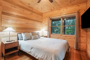 Une chambre à coucher dans un chalet en bois, avec un lit, deux tables de chevet, des lampes et une grande fenêtre avec des rideaux.