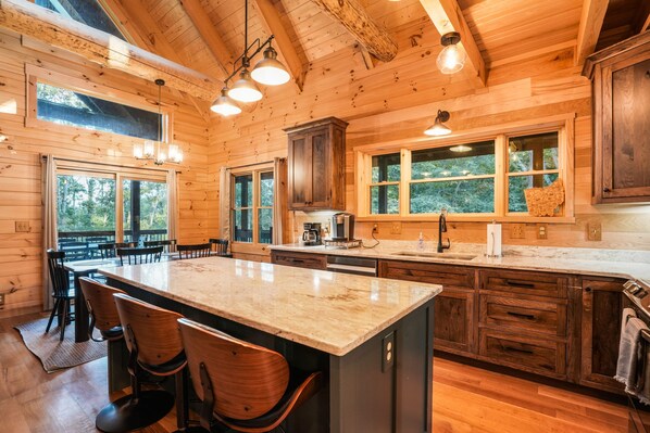 Une cabane en bois dotée d’une grande cuisine comprenant un îlot en marbre, des tabourets de bar et des meubles de rangement en bois.