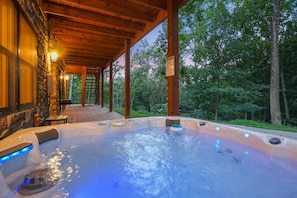 A hot tub area with a wooden deck, stone walls, and a view of the surrounding forest.