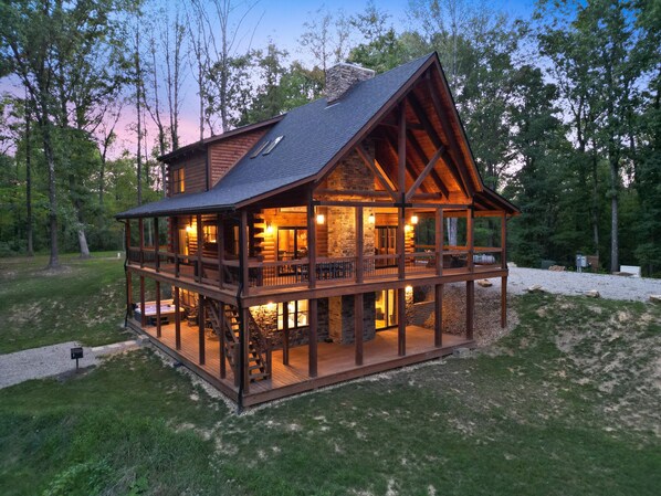 A log cabin with a wooden deck and multiple windows, surrounded by trees.