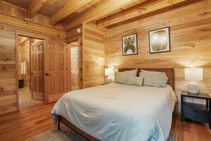 Un dormitorio con paneles de madera, una cama, mesitas de noche y una puerta que da a otra habitación.