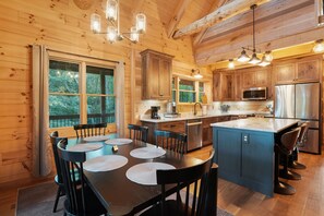 A wooden cabin interior with a dining area, kitchen, and large windows.
