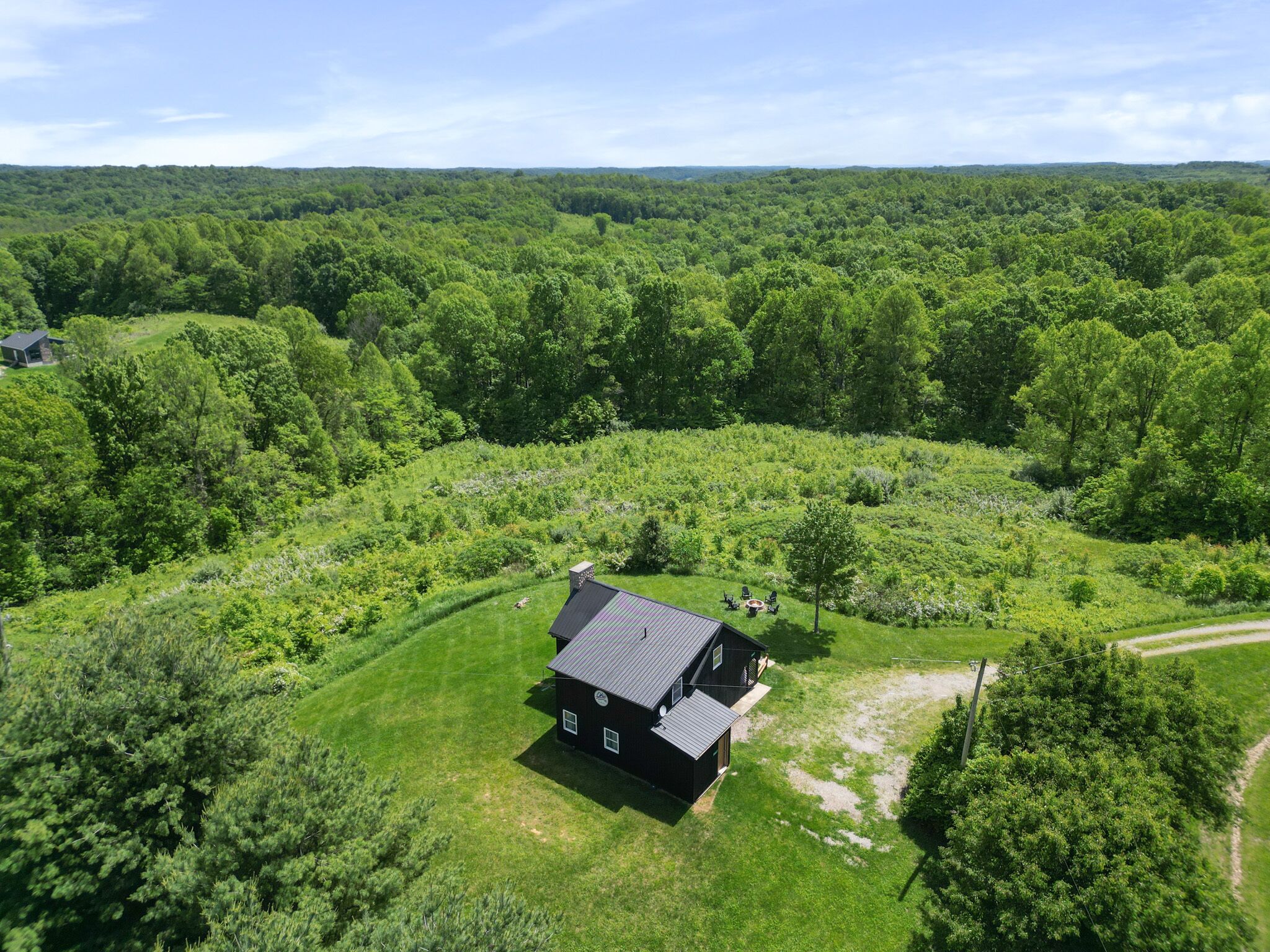 An aerial view of a house surrounded by lush greenery and a forested landscape.