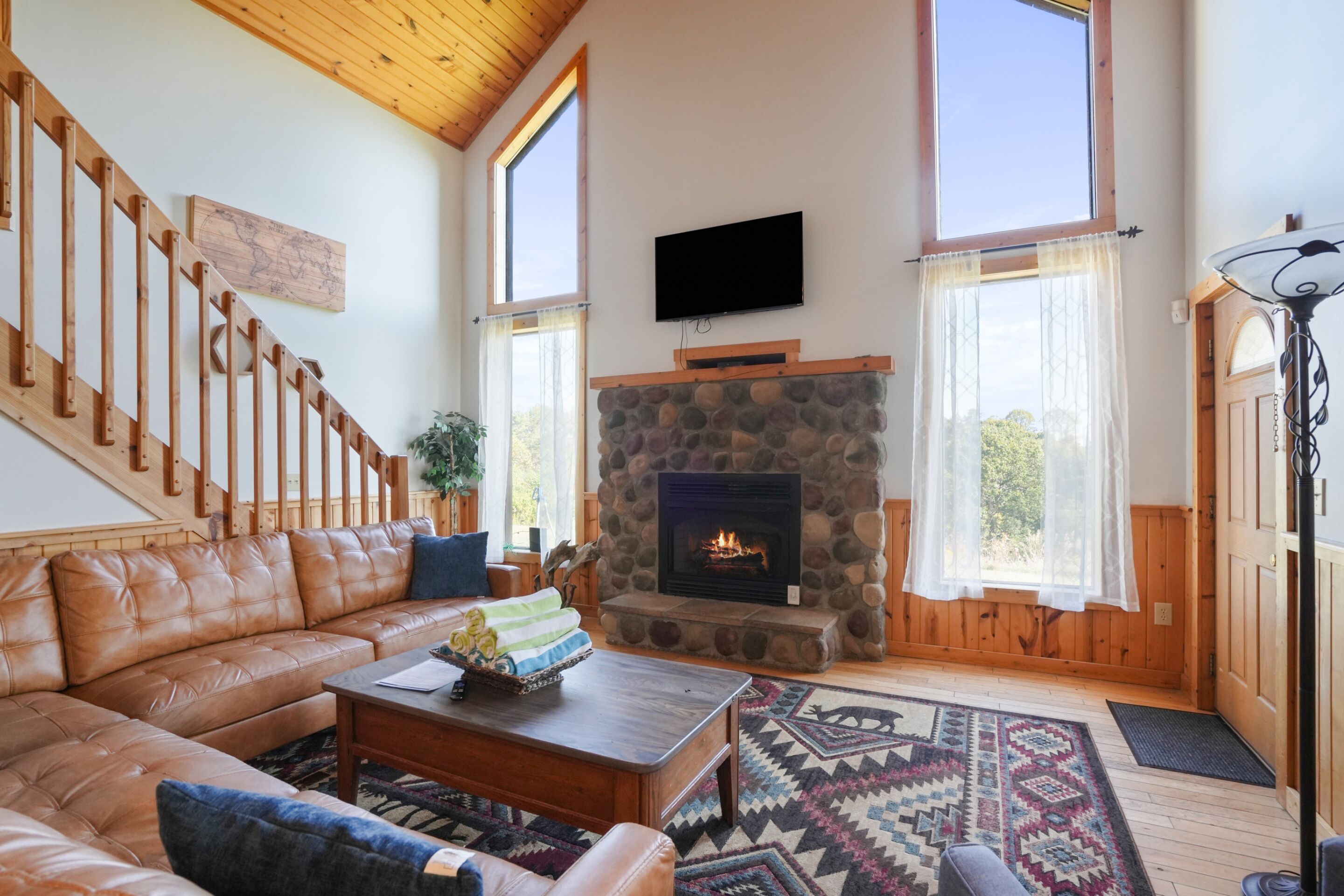 A spacious living room with a stone fireplace, leather sofa, and a wooden staircase.