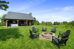 Eine Lodge mit einem Steinkamin, umgeben von Adirondack-Stühlen, einem überdachten Sitzbereich und einem gepflegten Rasen.