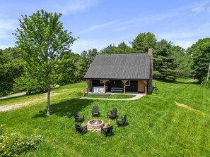 A lodge with a stone chimney, a fire pit, and outdoor seating.