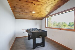A room with a wooden ceiling, a window with a view of trees, and a foosball table. - Hilltop Hideaway | Hocking Hills, 16 Acres (McArthur)