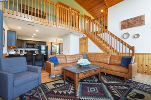 A spacious living area with a high wooden staircase, a leather sofa, a blue armchair, and a wooden coffee table.